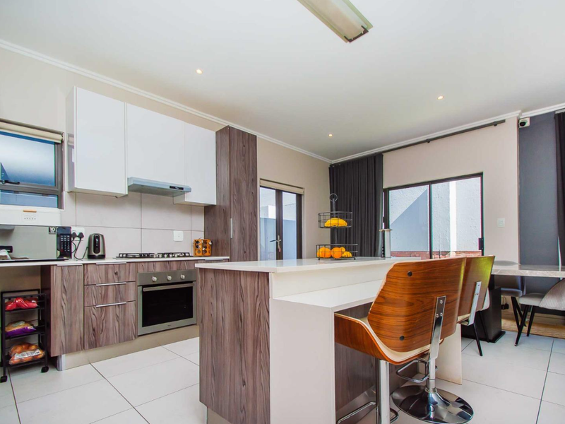Modern open-plan kitchen featuring two-tone cabinetry, a central island with breakfast bar, gas hob, and direct access to the outdoor area.