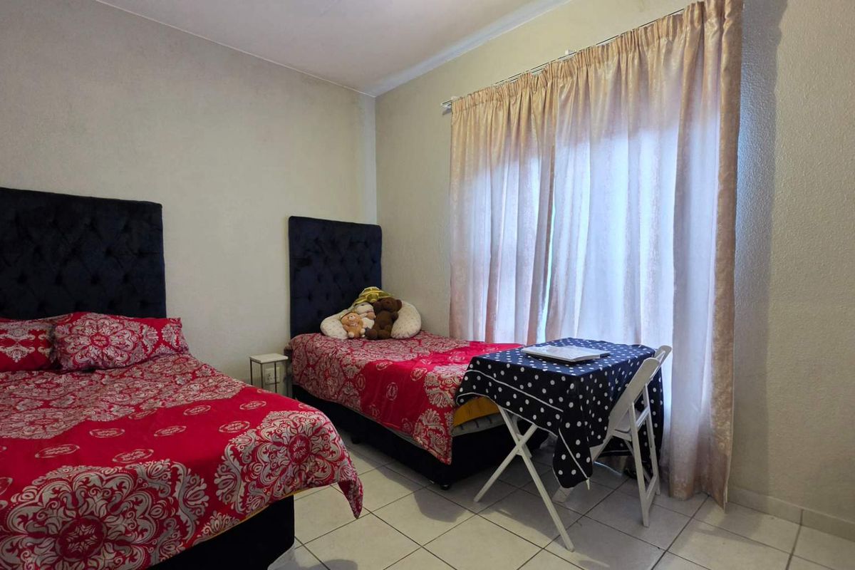 A bedroom featuring tiled flooring and a large window with curtains, providing natural light to the space.