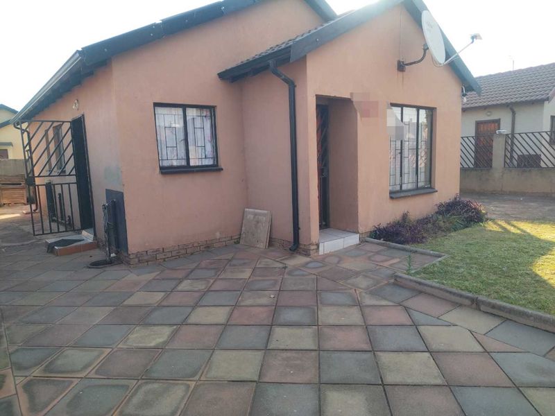 Front view of a single-story house featuring a paved patio area, security gates, burglar bars, and a tiled roof.