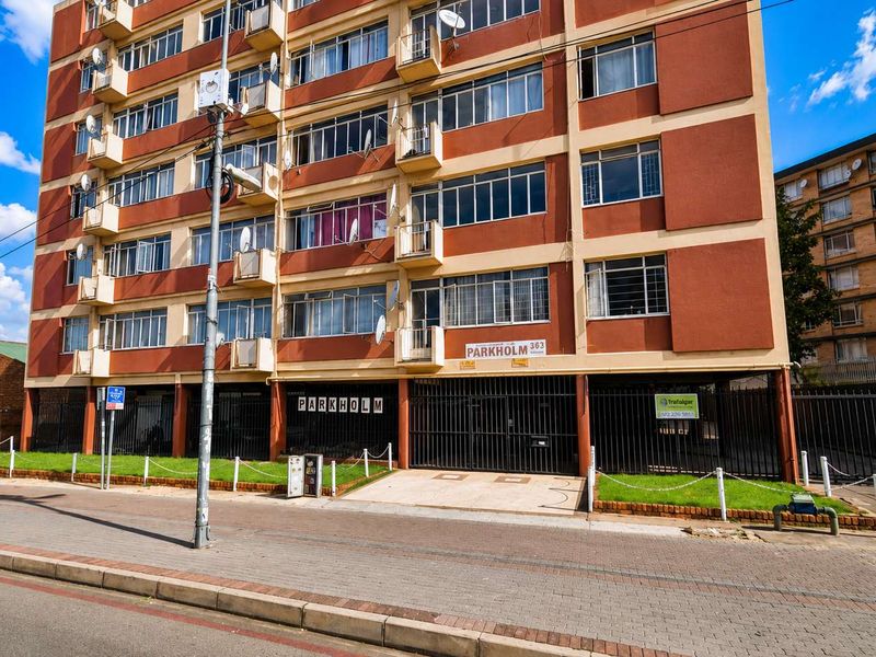 Front exterior view of Parkholm apartment building, featuring a multi-story facade with balconies, secure gated parking access, and landscaped street-level frontage.