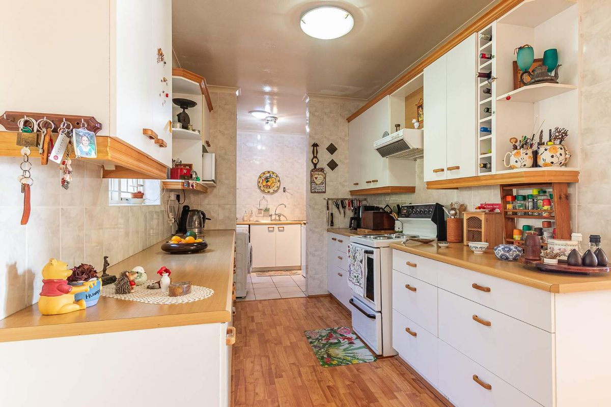 A functional galley-style kitchen featuring white cabinetry, wood-look laminate countertops, tiled splashbacks, and a dedicated scullery area at the rear.