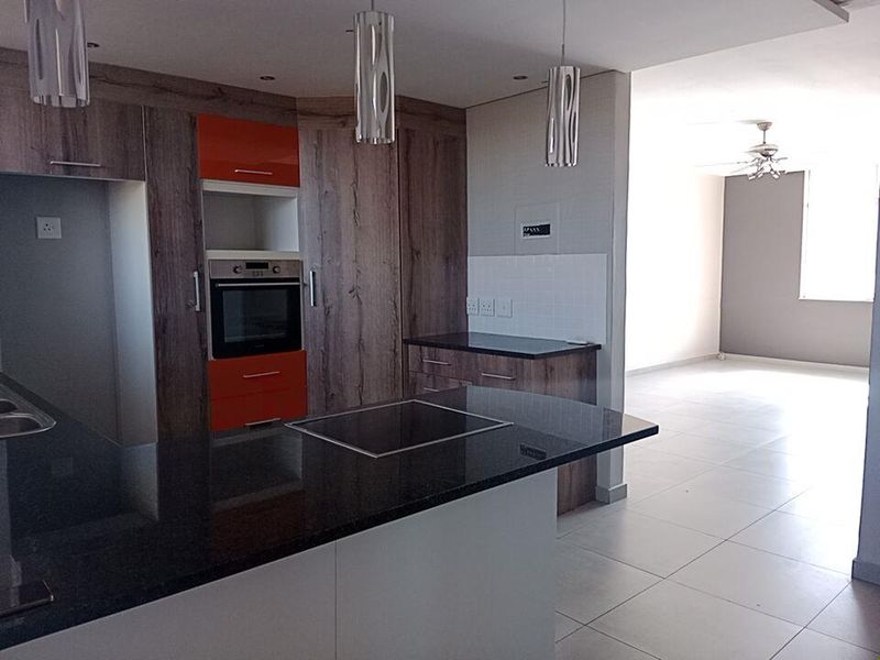 Modern open-plan kitchen featuring granite countertops, built-in oven, and sleek cabinetry, flowing into a spacious, tiled living area with a ceiling fan.