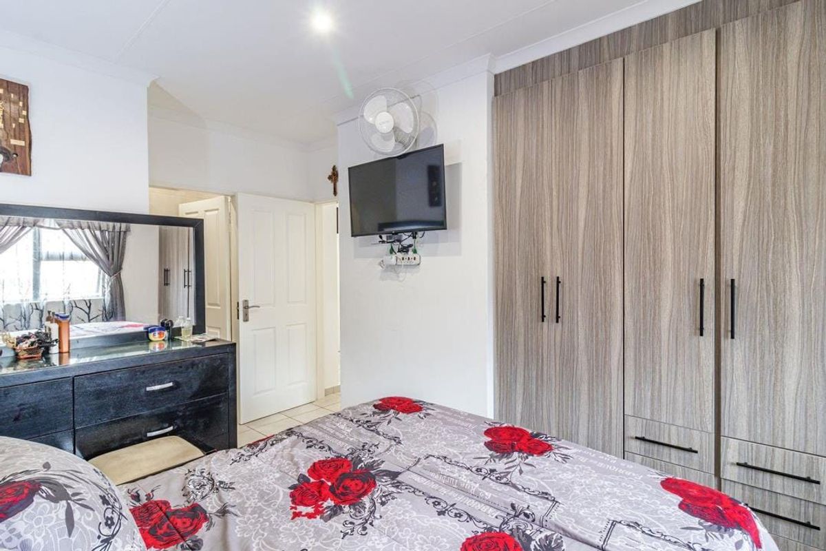 A well-maintained bedroom featuring modern wood-grain built-in cupboards, tiled flooring, and a ceiling fan, offering a functional and comfortable living space.