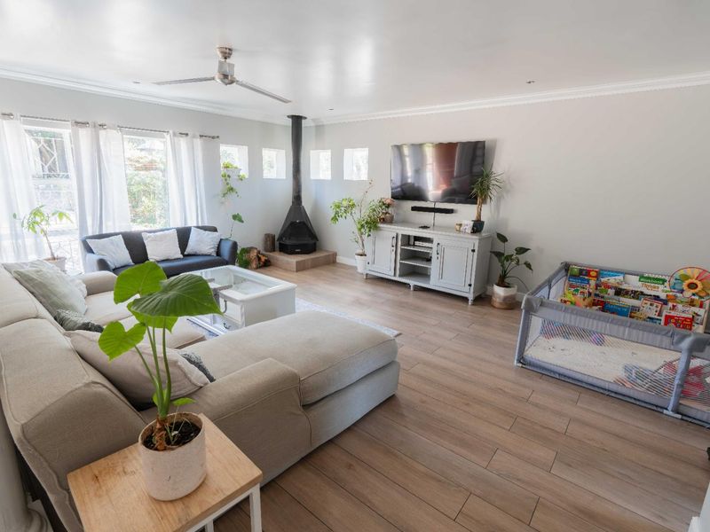 Spacious living room featuring light-toned laminate flooring, a modern wood-burning fireplace, and a ceiling fan, creating a bright and comfortable family living space.