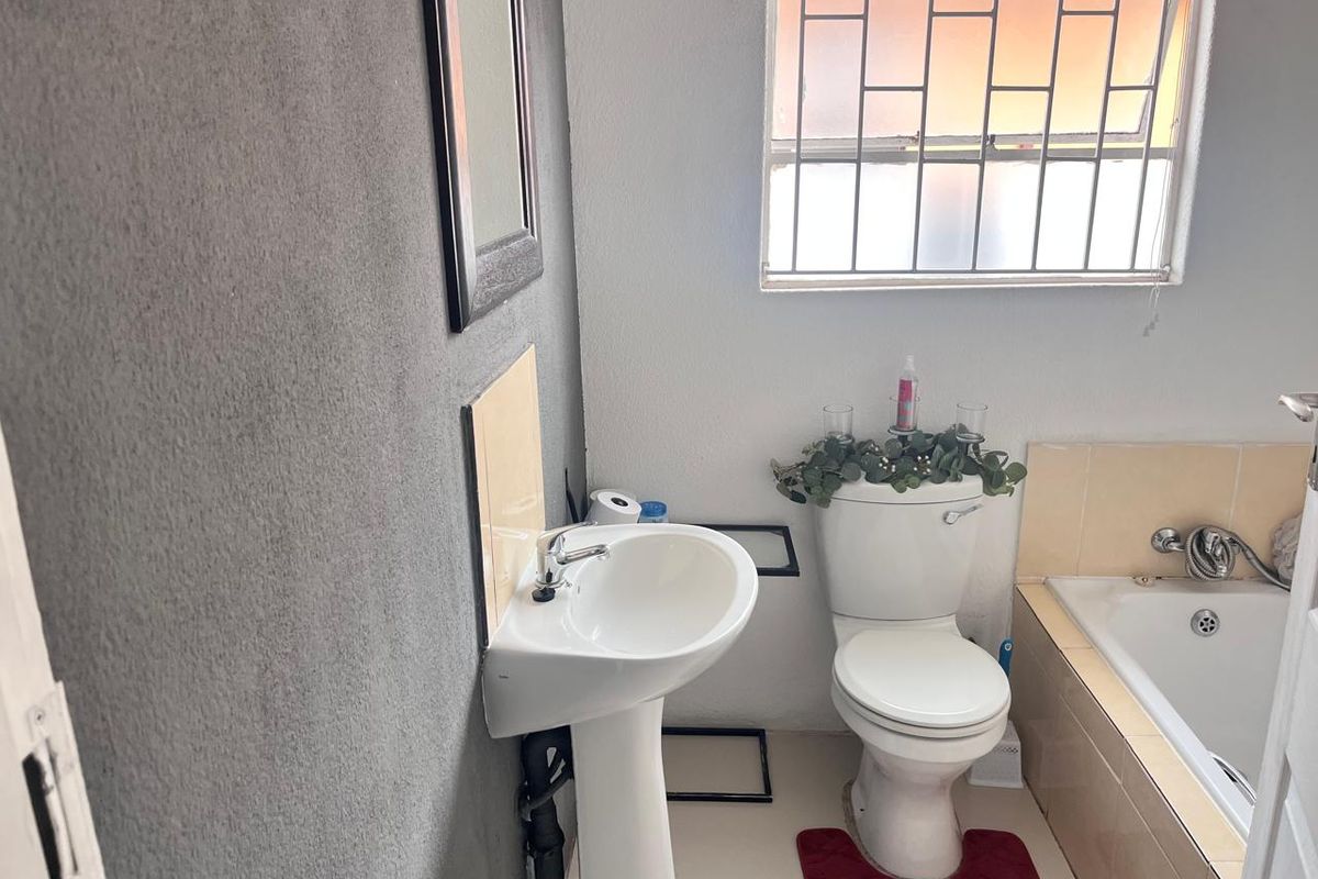 A functional bathroom featuring a pedestal basin, standard toilet, and a tiled bathtub with a security-barred window.