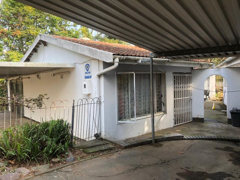Front exterior view of the property featuring a corrugated metal carport, security gates, and paved driveway area.