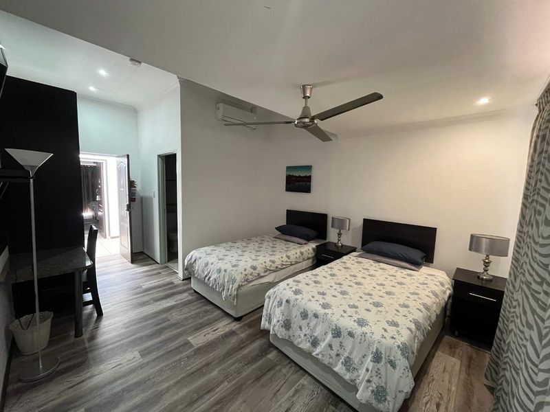 A well-maintained bedroom featuring modern laminate flooring, a ceiling fan, and a split-system air conditioner, with an adjoining en-suite bathroom.