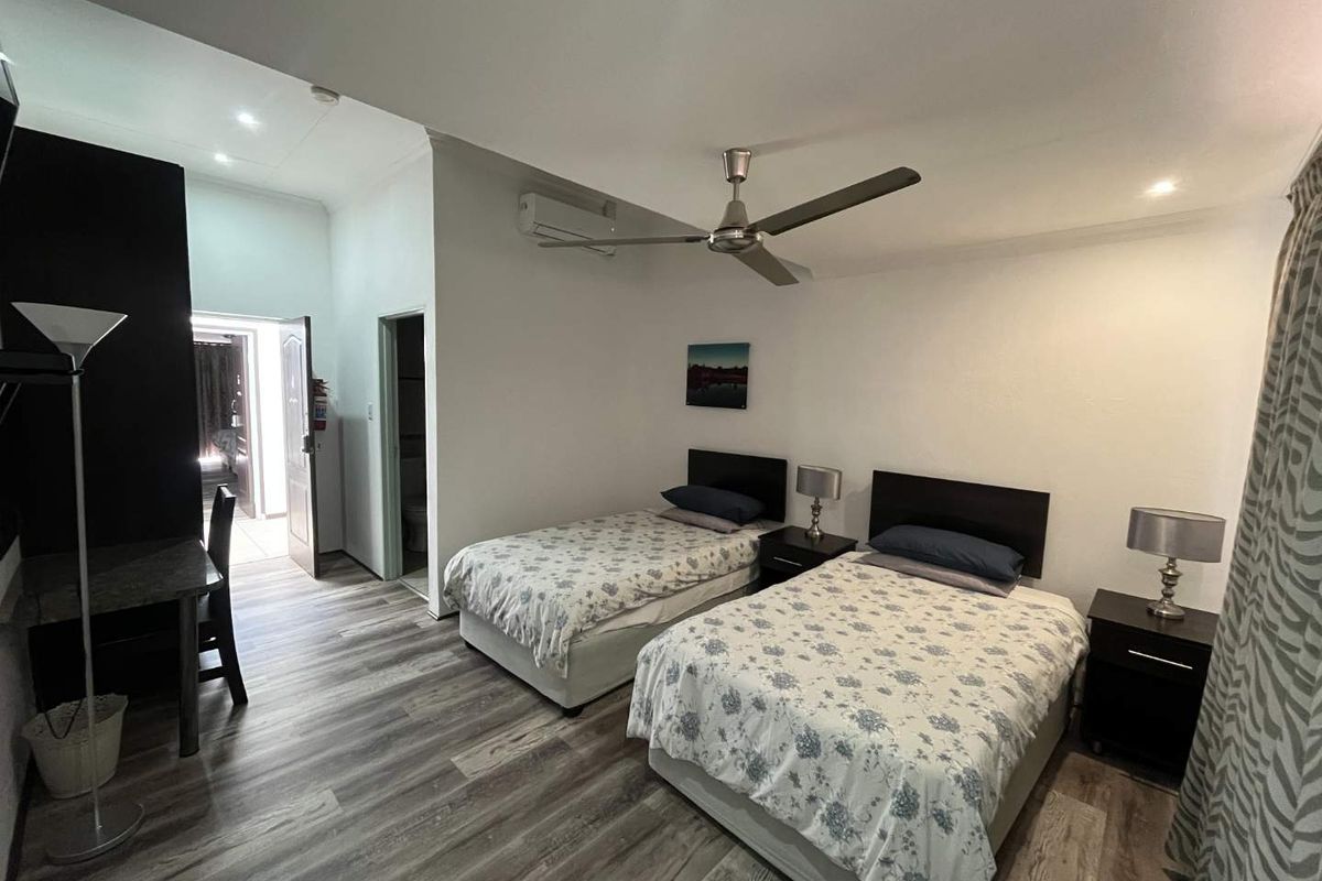 A well-maintained bedroom featuring modern laminate flooring, a ceiling fan, and a split-system air conditioner, with an adjoining en-suite bathroom.