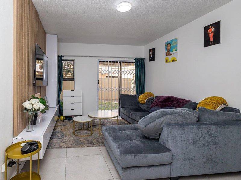 A well-maintained living room featuring tiled floors, a modern slatted wood accent wall, and a sliding glass door with security gate leading outdoors.
