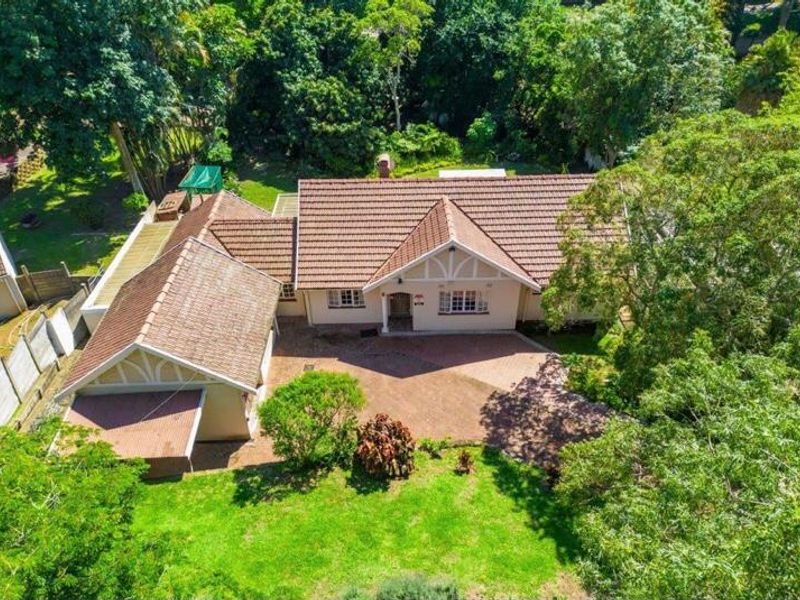 Aerial view of a single-story residential house featuring a tiled roof, brick paved driveway, and established garden surroundings.