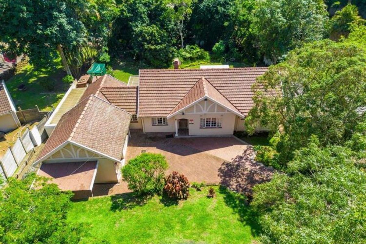 Aerial view of a single-story residential house featuring a tiled roof, brick paved driveway, and established garden surroundings.