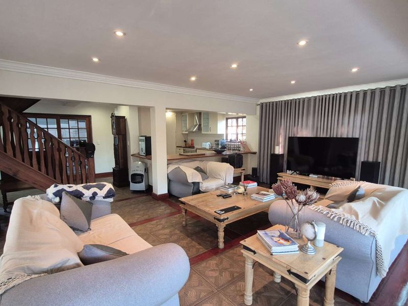 Spacious open-plan living area featuring a kitchen with breakfast bar, tiled flooring, recessed lighting, and an integrated wooden staircase.