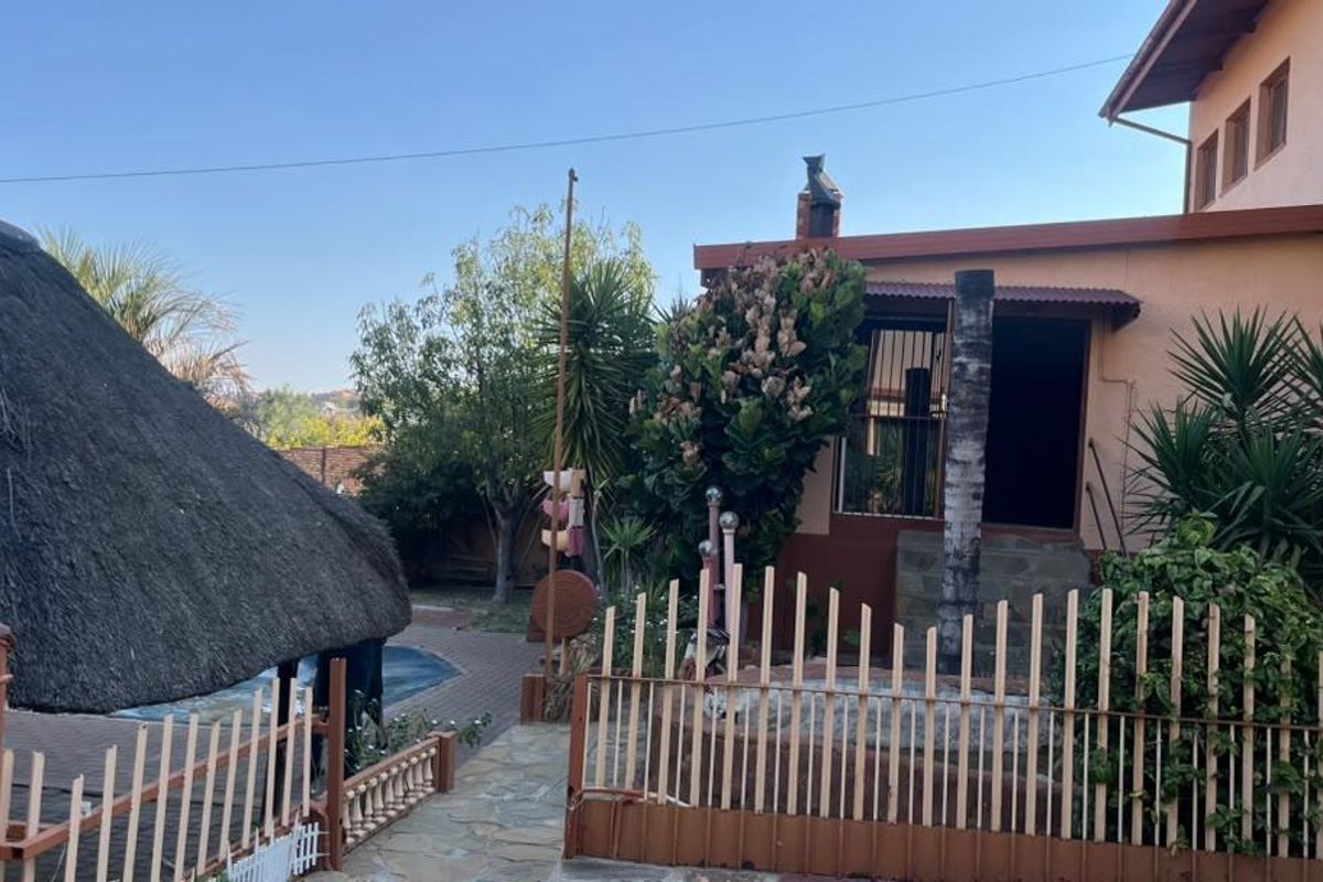 Rear exterior view featuring a thatch roof lapa, swimming pool, paved patio area, and perimeter fencing.