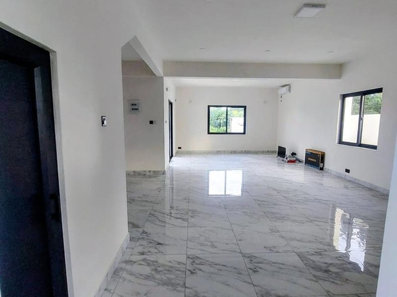 A spacious, open-plan living area featuring polished marble-look floor tiles, recessed lighting, and modern black-framed windows.