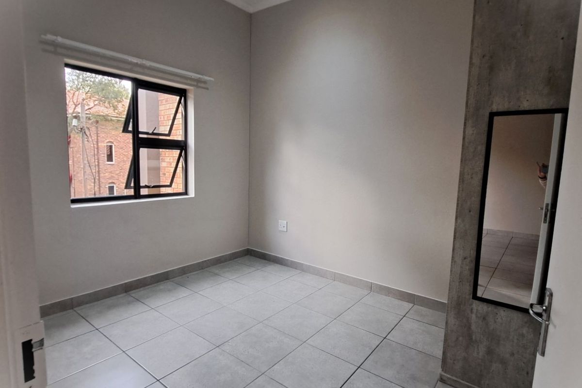 A clean, empty bedroom featuring neutral tiled flooring, a modern concrete-look accent wall, and a window providing natural light.