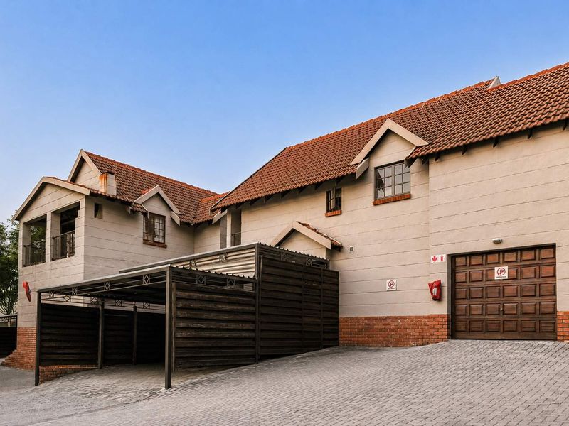 Front exterior view of a townhouse featuring a paved driveway, integrated garage, and covered carport with a tiled roof and brick accents.