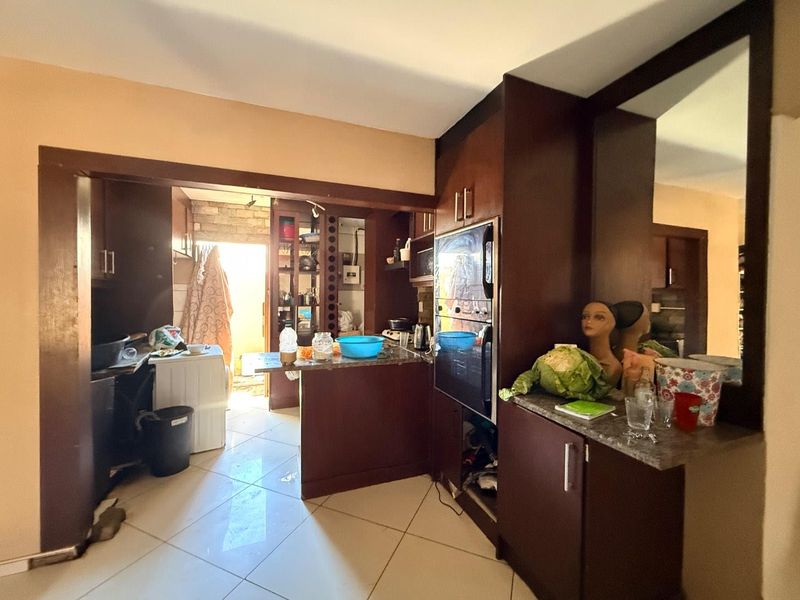 A dated kitchen featuring dark wood cabinetry, granite countertops, and built-in appliances, with an open-plan layout leading to a utility area.
