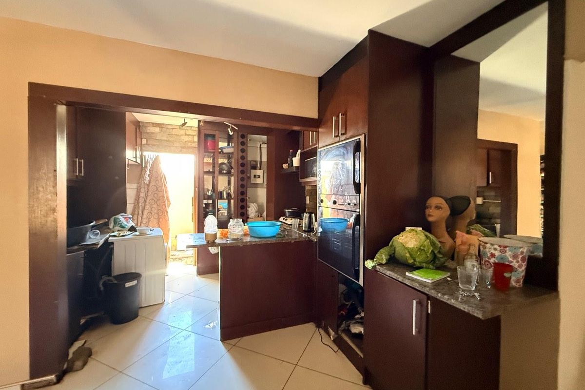 A dated kitchen featuring dark wood cabinetry, granite countertops, and built-in appliances, with an open-plan layout leading to a utility area.