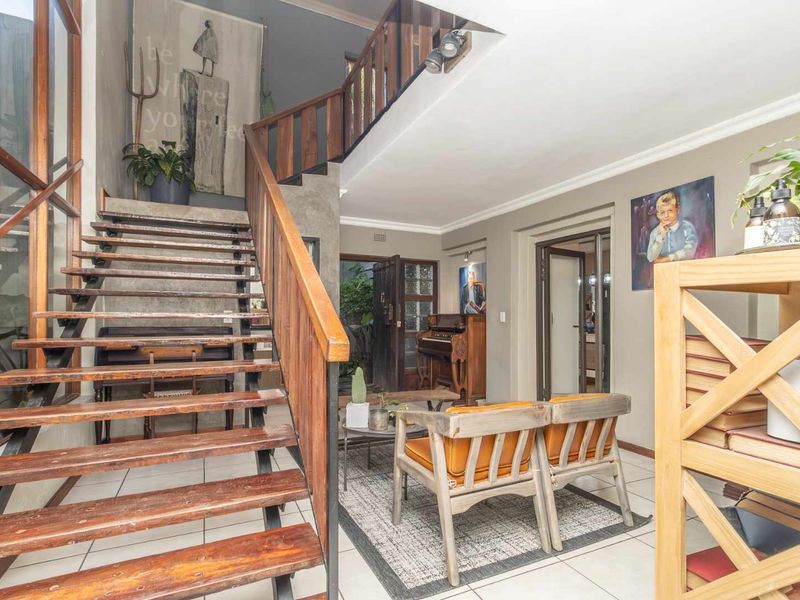 Spacious living area featuring an open-tread timber staircase, tiled flooring, and double-volume ceilings, creating an airy and architectural atmosphere.