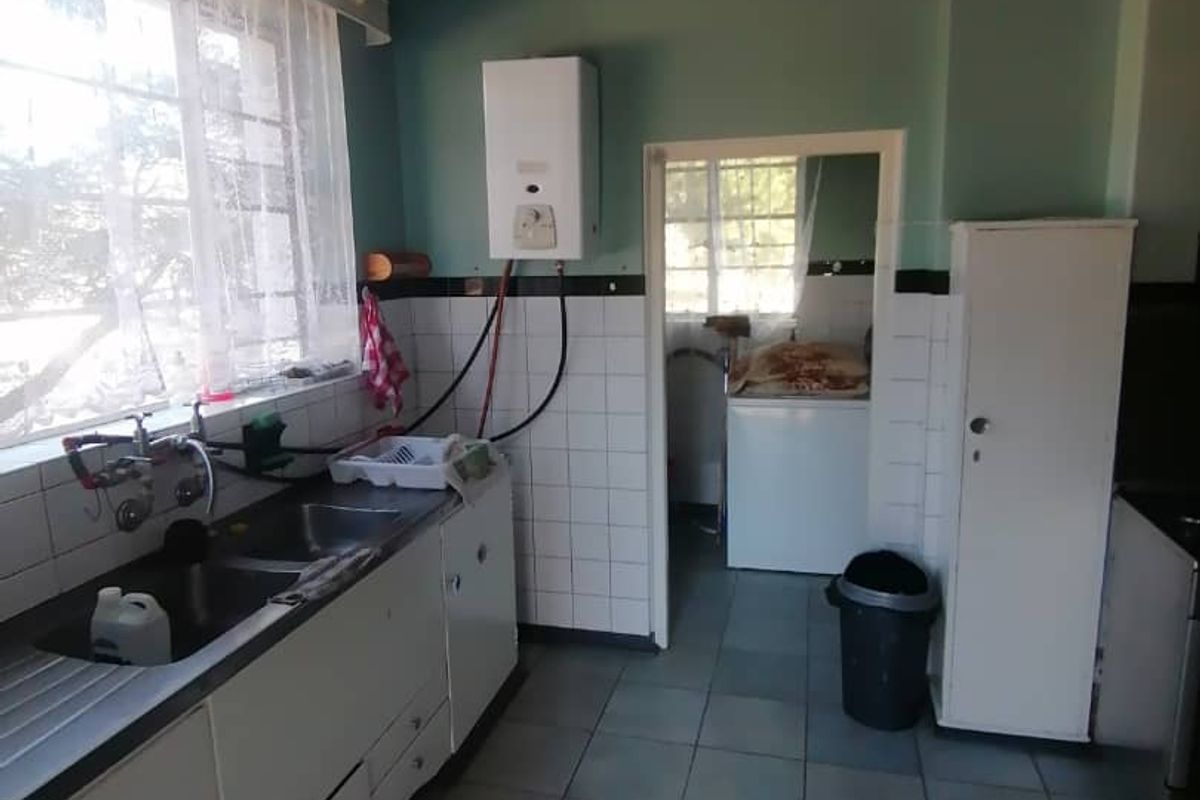 A functional kitchen featuring built-in cabinetry, a double sink, and a wall-mounted gas geyser, with an adjacent scullery area.