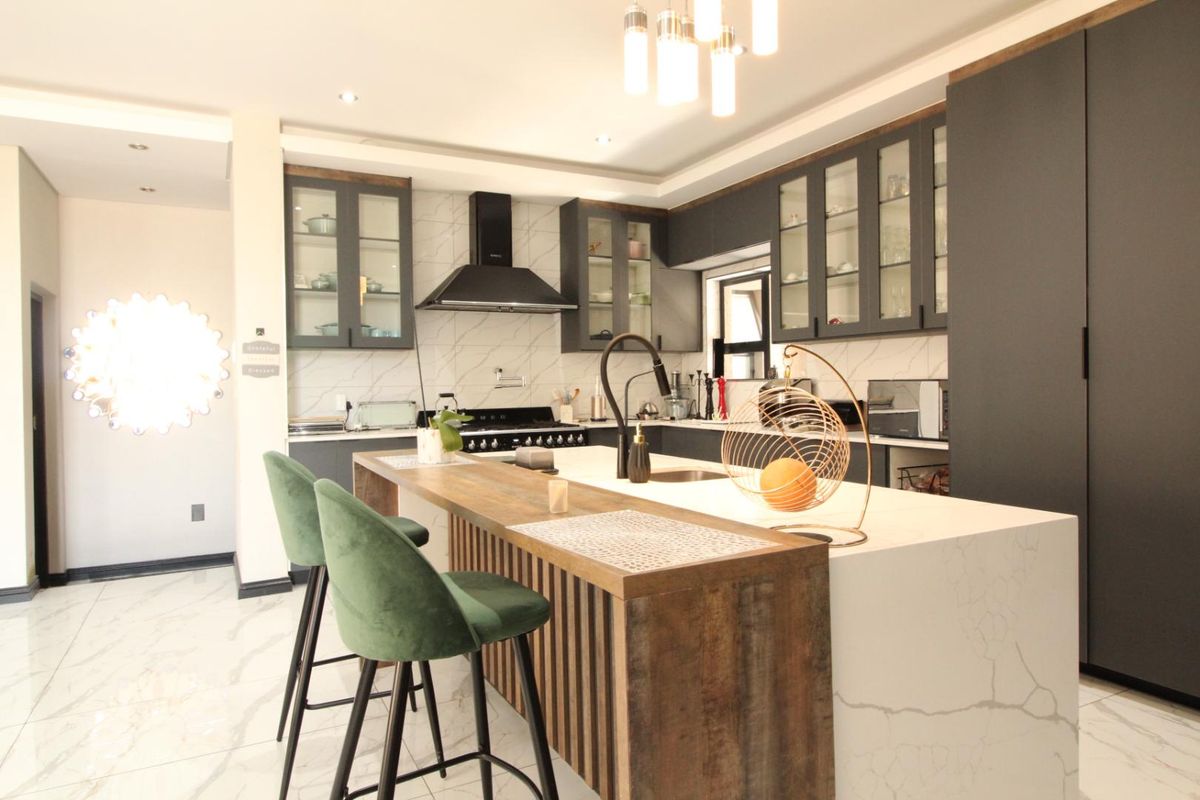 Modern kitchen featuring dark cabinetry, a large stone-topped island with integrated sink, marble-look flooring, and high-end built-in appliances.