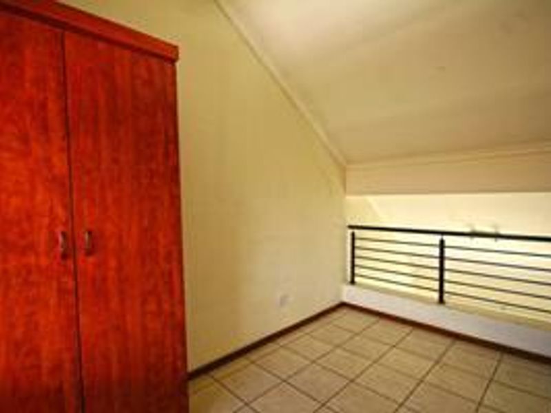 An empty bedroom featuring tiled flooring, a built-in wooden wardrobe, and a metal balustrade overlooking the lower level.