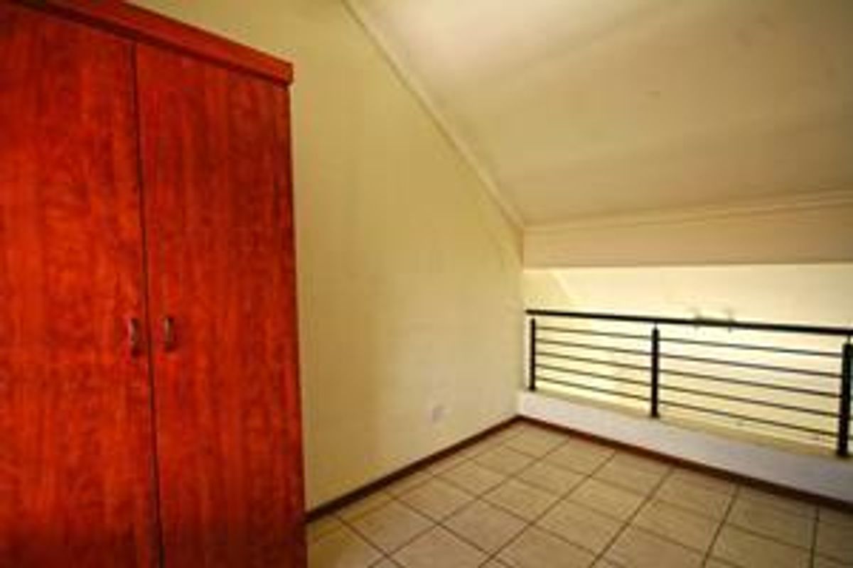 An empty bedroom featuring tiled flooring, a built-in wooden wardrobe, and a metal balustrade overlooking the lower level.