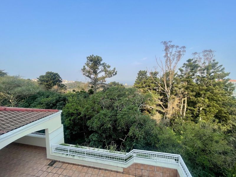 A spacious balcony featuring tiled flooring and a metal balustrade, offering an elevated view over the surrounding lush greenery and trees.
