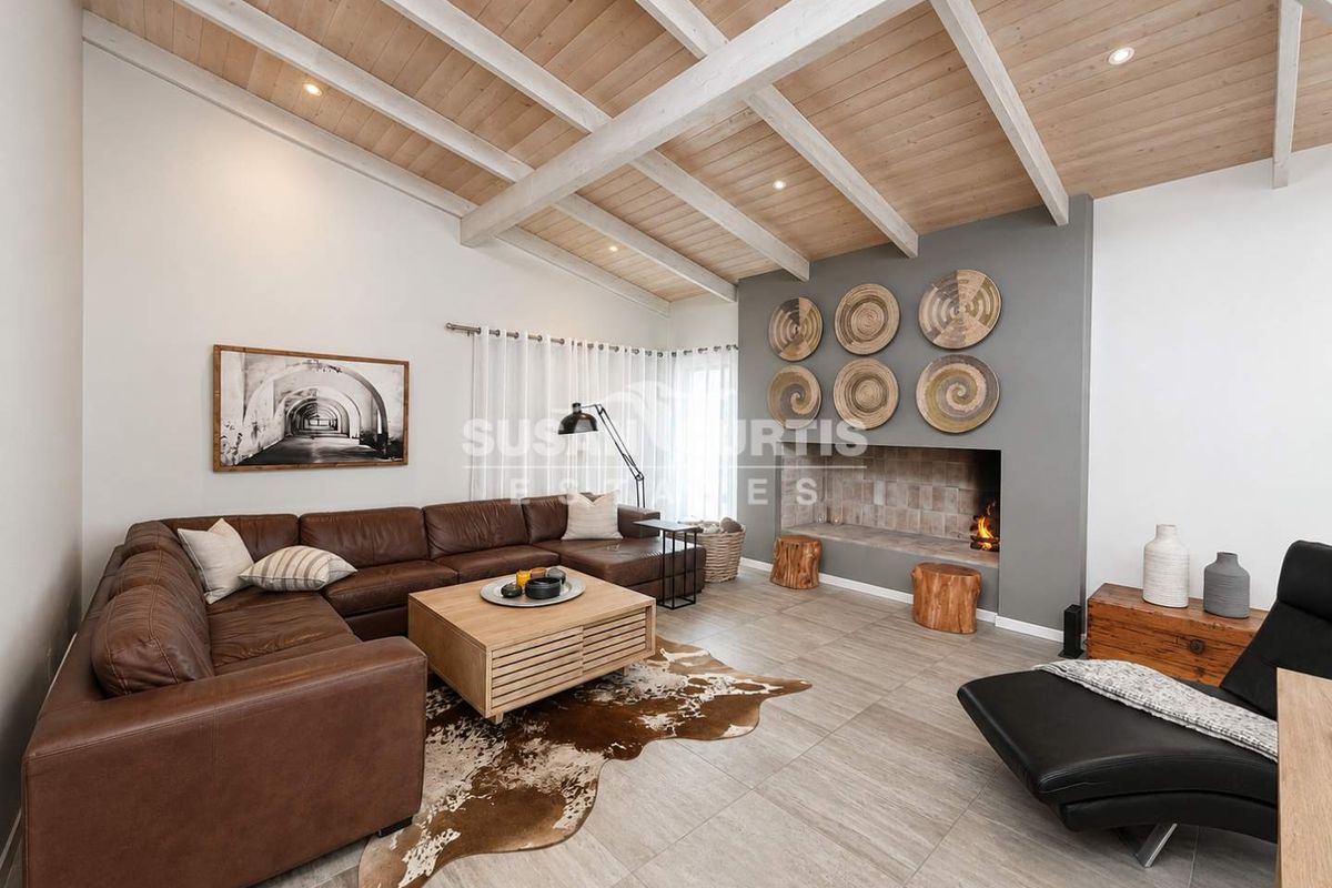 Spacious living room featuring a vaulted timber ceiling with exposed beams, tiled flooring, and a modern built-in fireplace as a central focal point.