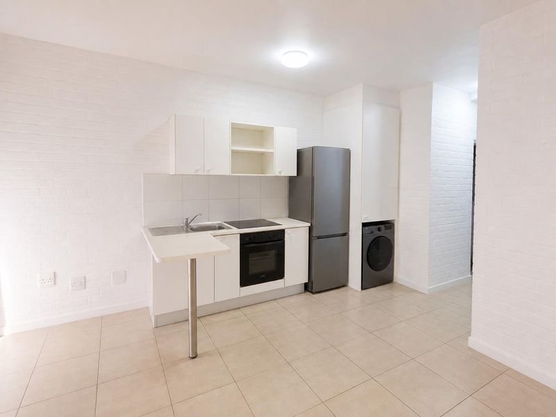 A clean, functional kitchen featuring white cabinetry, built-in oven and hob, stainless steel sink, and tiled flooring with an integrated breakfast bar.
