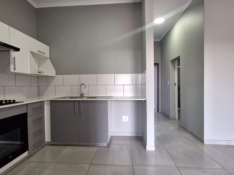 Modern kitchen featuring sleek grey and white cabinetry, built-in oven and hob, tiled backsplash, and neutral floor tiles in an open-plan layout.