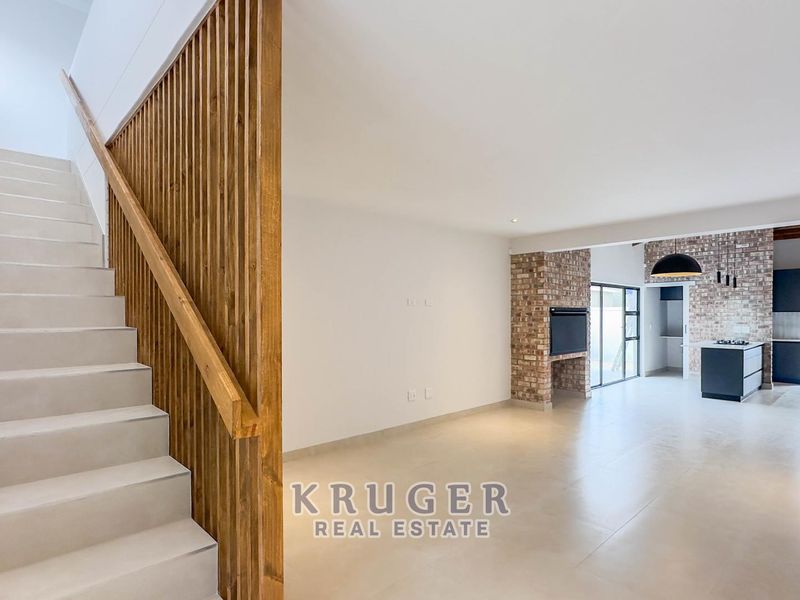 Spacious open-plan living area featuring a modern staircase with timber slat balustrade, exposed brick fireplace, and a contemporary kitchen with island.