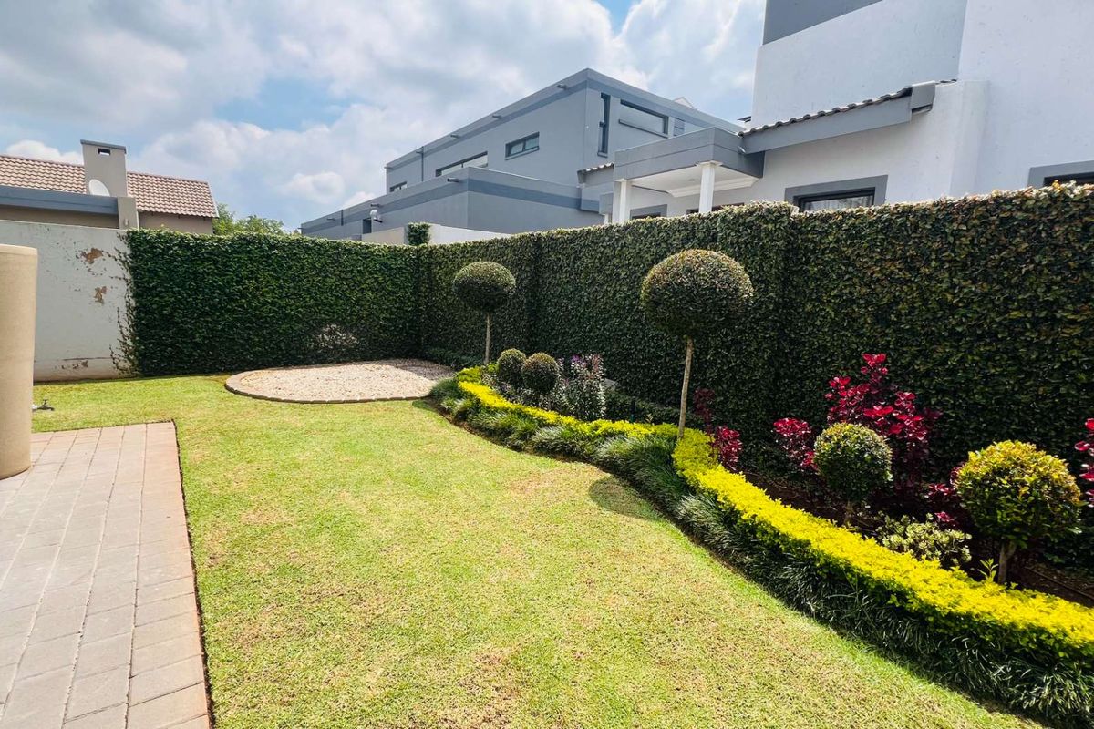 A well-maintained rear garden featuring a paved patio, manicured lawn, structured hedging, and a decorative gravel area.