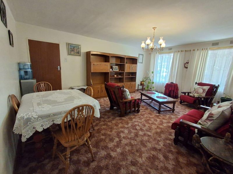 Spacious living room featuring a built-in wooden shelving unit, traditional chandelier lighting, and wall-to-wall carpeting.