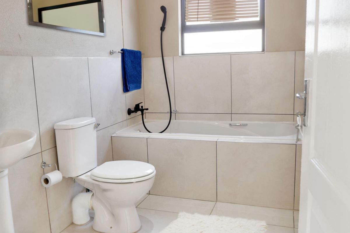 A clean, modern bathroom featuring neutral wall and floor tiles, a built-in bathtub with a handheld shower attachment, and a standard toilet.
