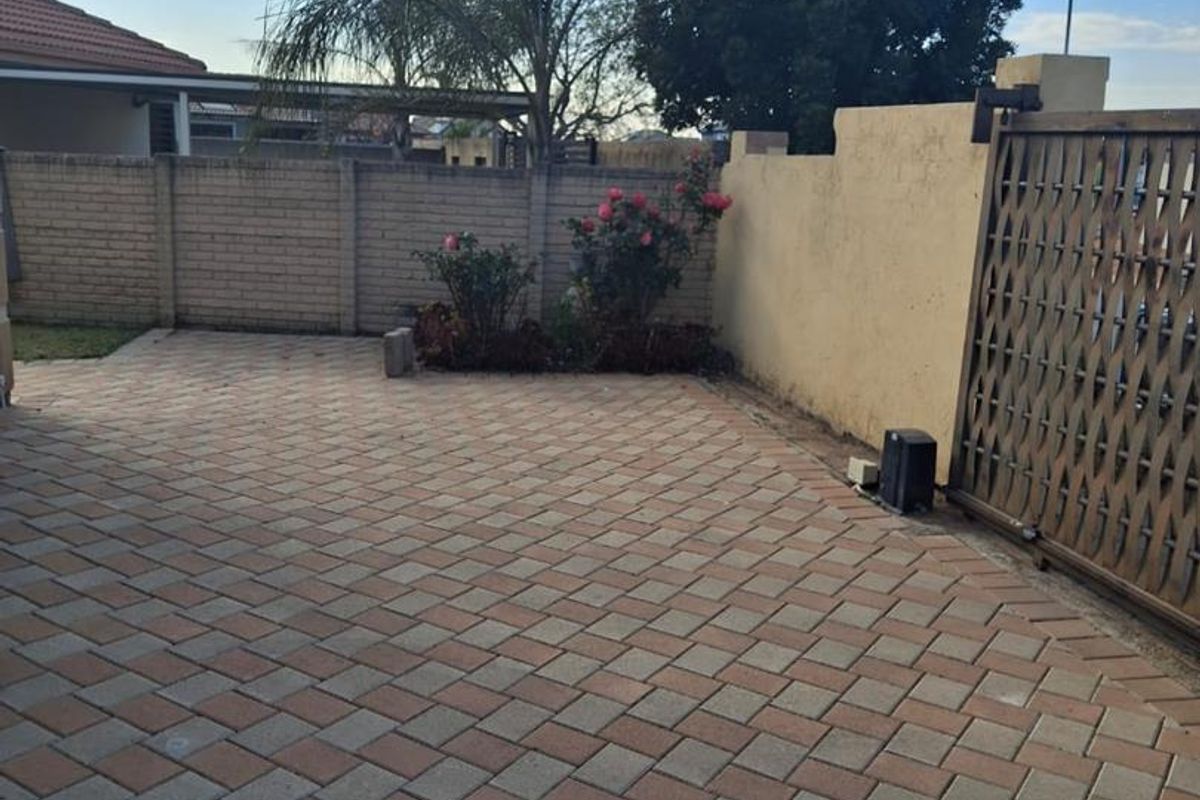 A paved rear courtyard area featuring a brick boundary wall, plastered wall, and a secure sliding gate.