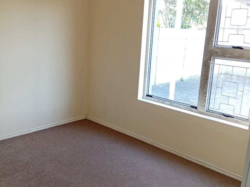 An empty bedroom featuring neutral walls, carpet flooring, and an aluminium-framed window with a curtain rail.