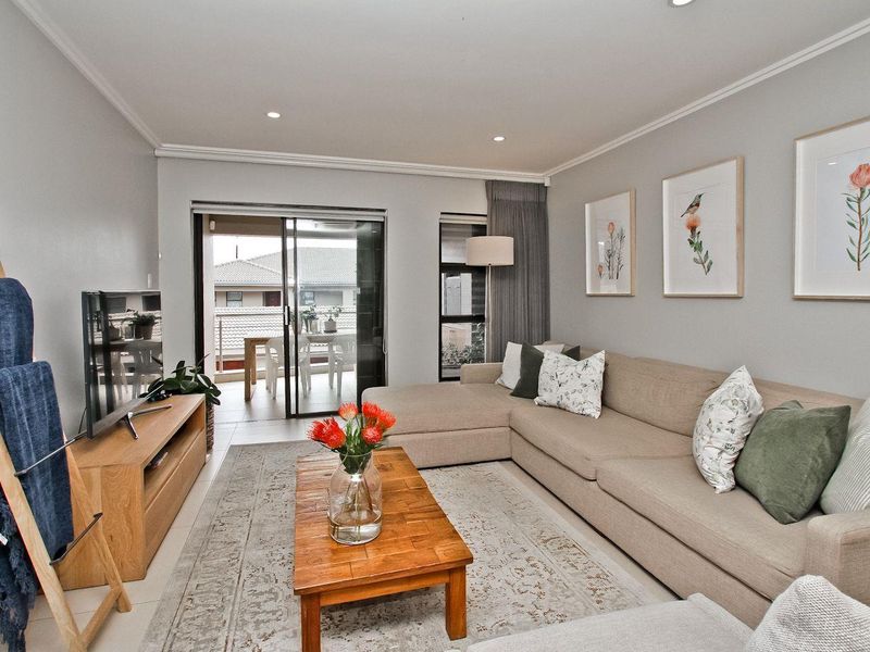 A well-maintained living room featuring tiled flooring, recessed downlights, and a sliding glass door providing access to an outdoor balcony area.