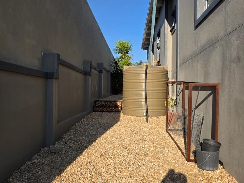 A side passage of the property featuring a gravel ground cover, a water storage tank, and a high boundary wall.