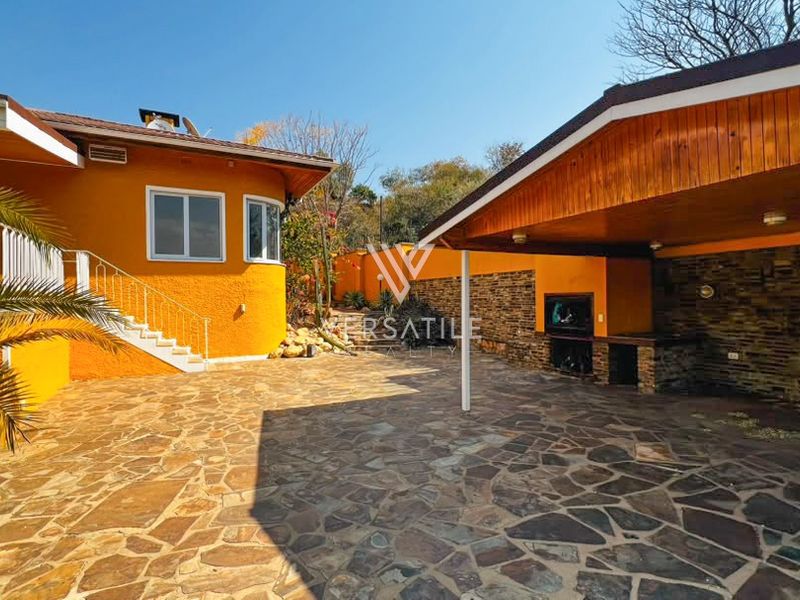 Spacious outdoor entertainment area featuring a covered patio with a built-in braai, stone paving, and attractive stone-clad feature walls.