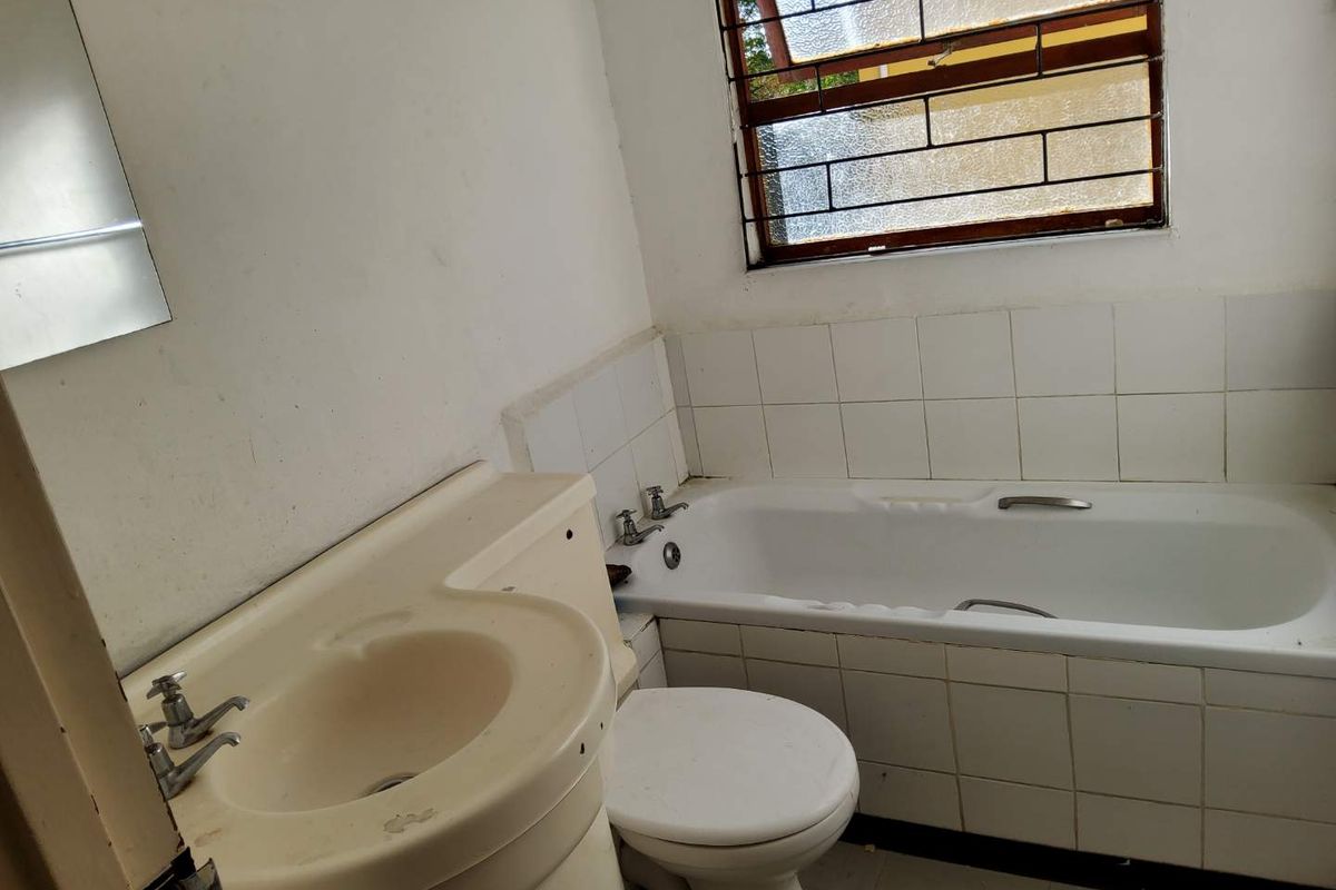 A dated bathroom featuring a built-in vanity, standard bathtub, and toilet with tiled splashbacks and a security-barred window.