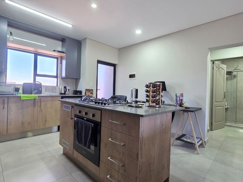 Modern kitchen featuring a central island with a built-in oven and gas hob, complemented by sleek cabinetry and high-quality tiled flooring.