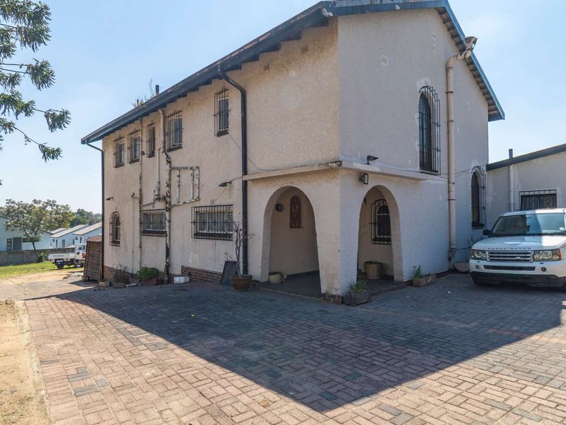Front exterior view of a two-story house featuring a paved driveway, arched entrance, and security bars on windows.
