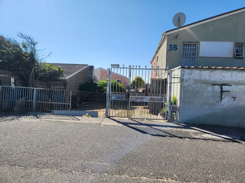 Front exterior view of the property featuring a metal security gate, perimeter fencing, and a concrete driveway with visible signs of wear.