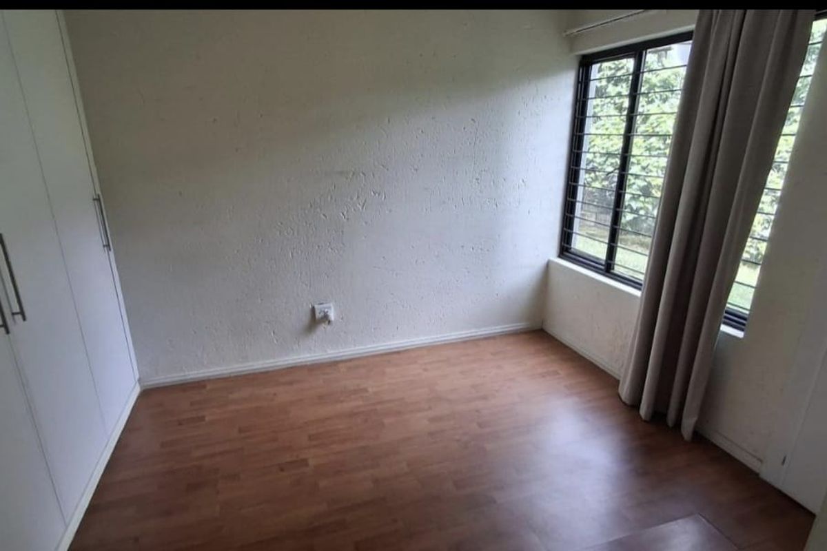 A vacant bedroom featuring laminate flooring, built-in cupboards, and a window fitted with security bars.