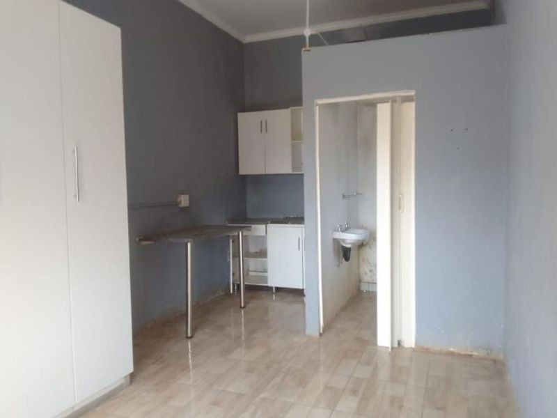 An open-plan studio space featuring tiled flooring, built-in wardrobe, basic kitchen cabinetry, and an integrated bathroom area with a wall-mounted basin.