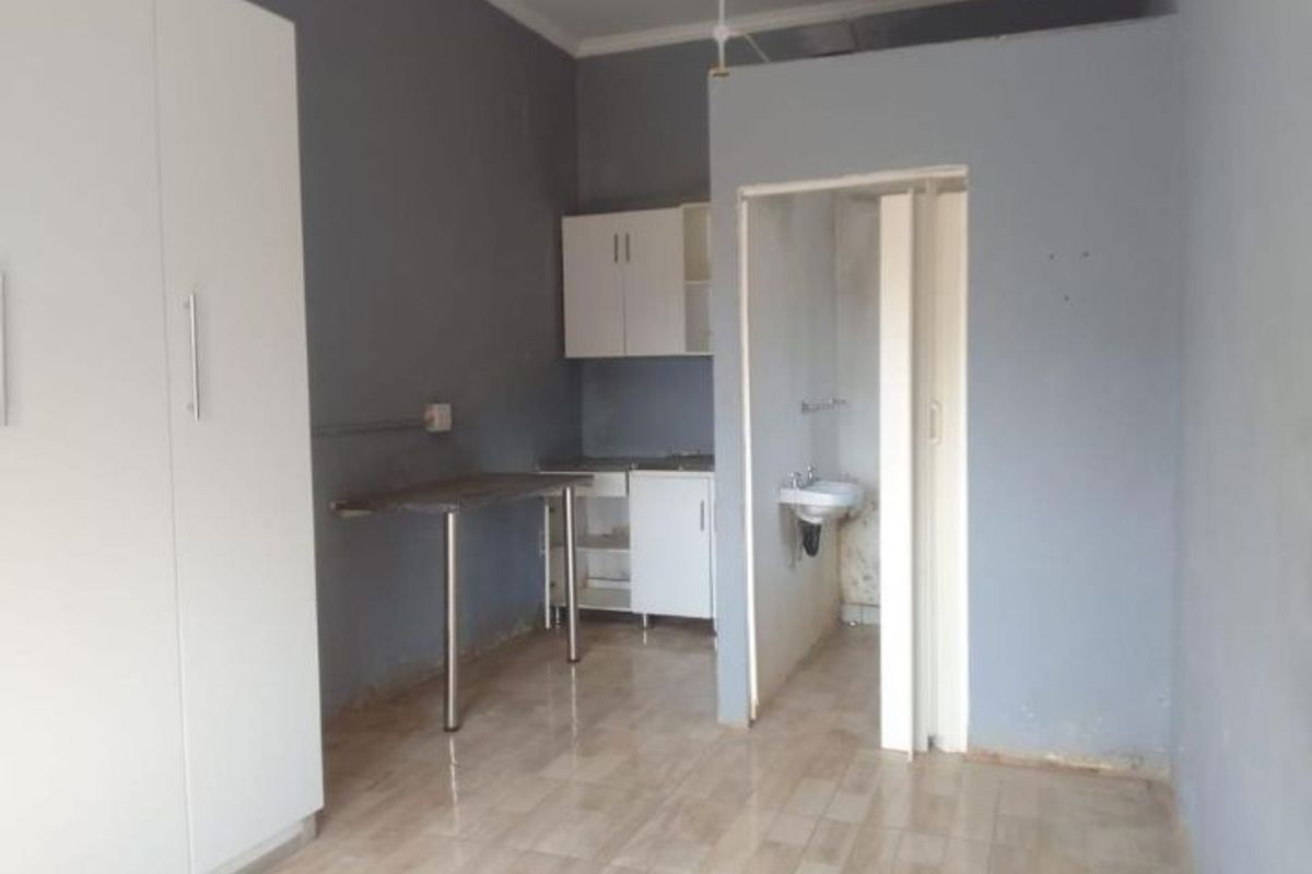 An open-plan studio space featuring tiled flooring, built-in wardrobe, basic kitchen cabinetry, and an integrated bathroom area with a wall-mounted basin.