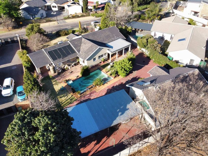 Aerial view of a residential property featuring a swimming pool, solar panels, covered patio, and paved driveway with carport.