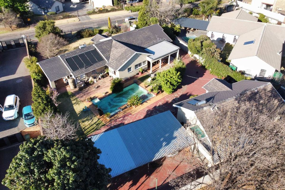 Aerial view of a residential property featuring a swimming pool, solar panels, covered patio, and paved driveway with carport.