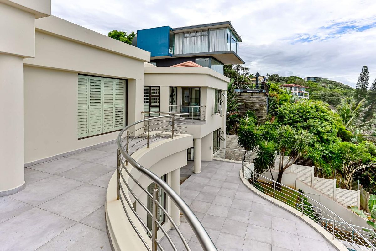 Spacious rear terrace featuring modern tiled flooring, stainless steel balustrades, and access to the home through large sliding doors and louvre shutters.